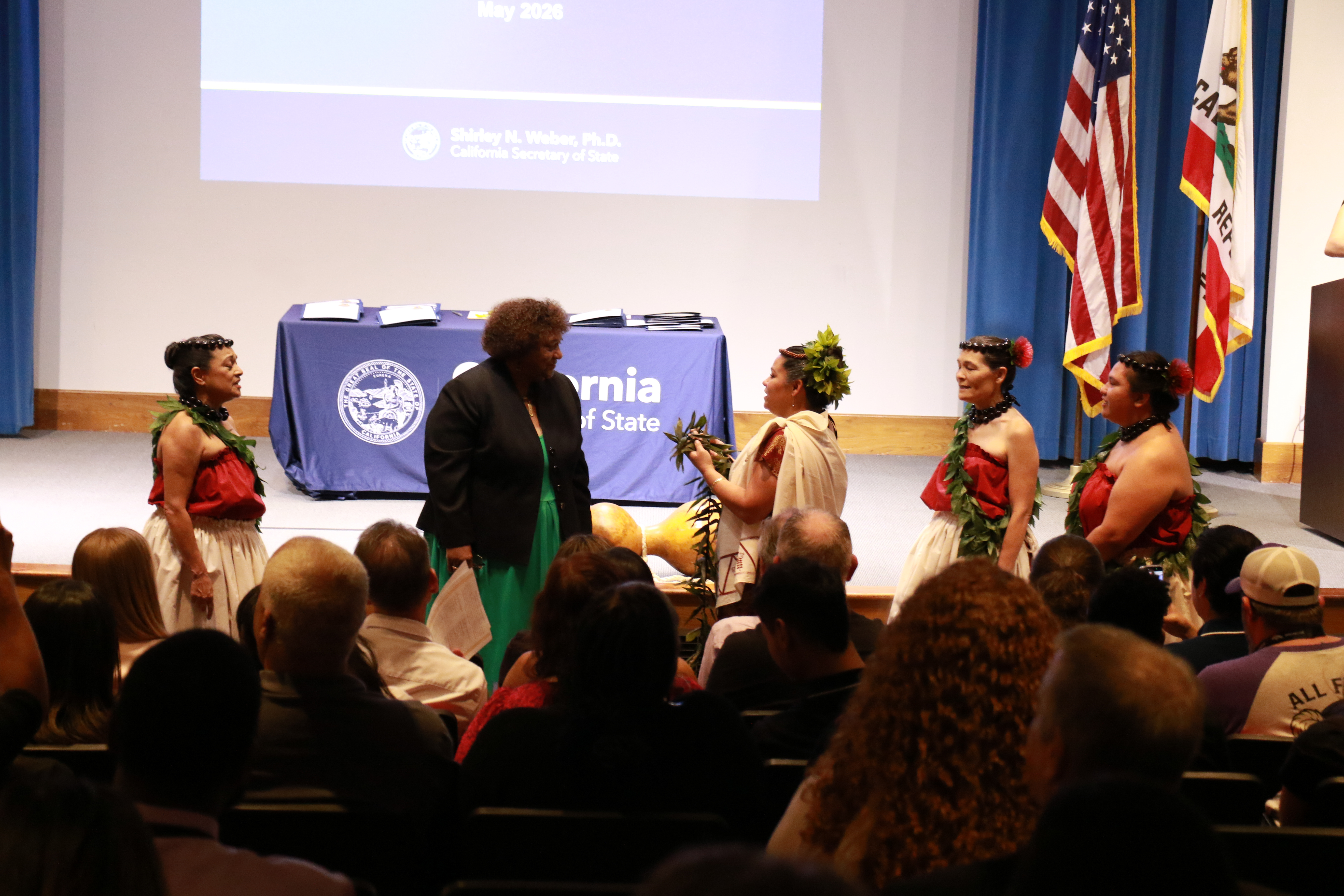 Secretary Weber being presented with a traditional tea leaf lei by four dancers, in front of the audience.